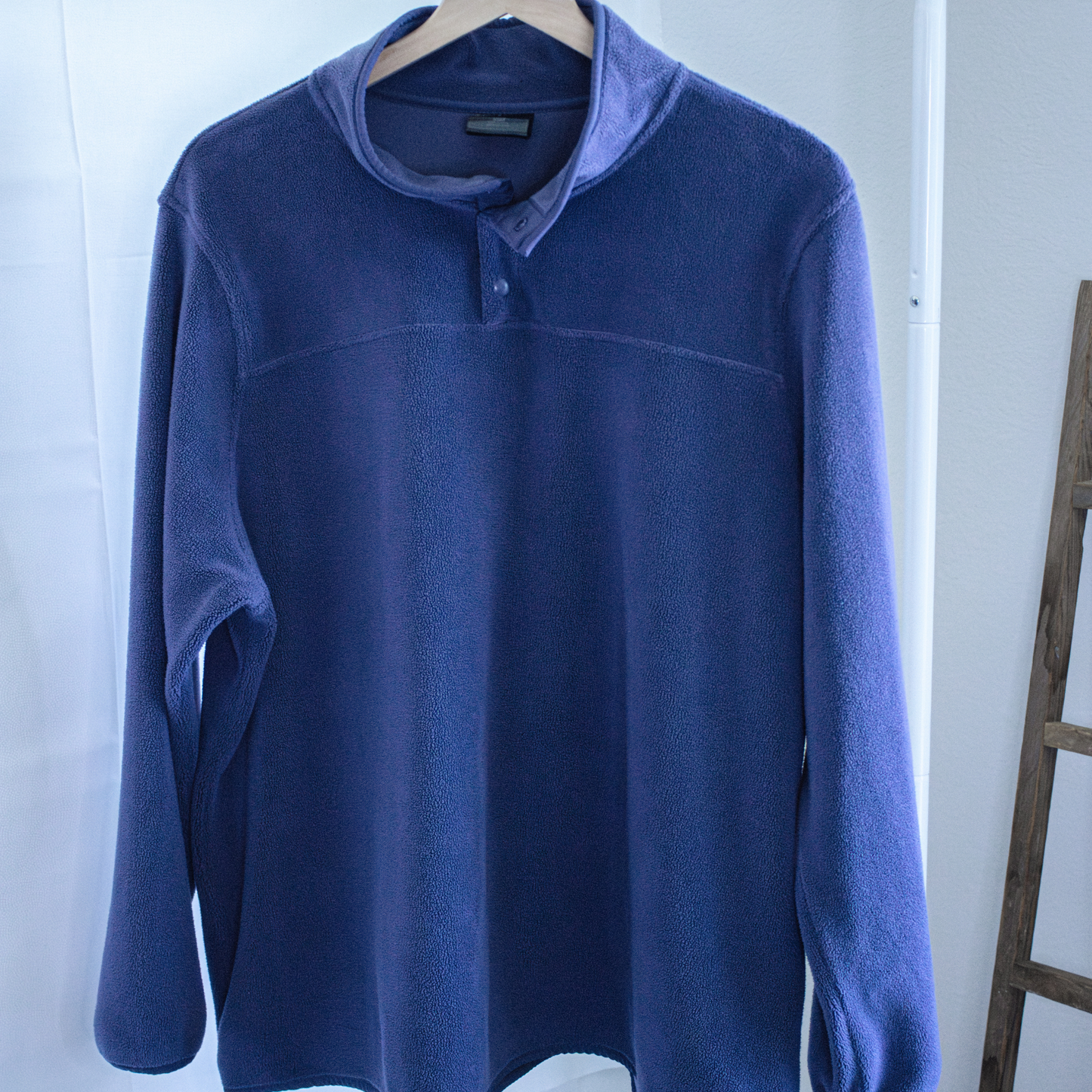 Blue fleece pullover on a hanger against a white wall