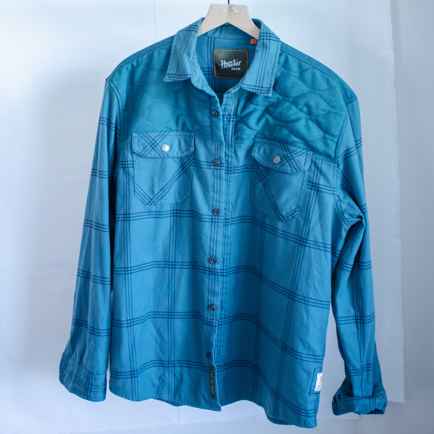 Howler Bros blue plaid shirt on a hanger against a white background