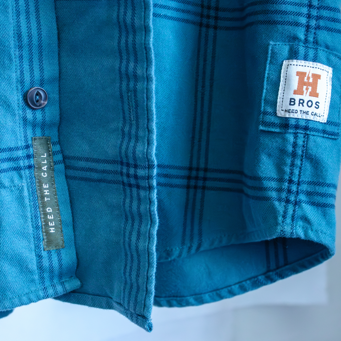 Close-up of a Howler Bros blue plaid shirt with a brand label on a white background