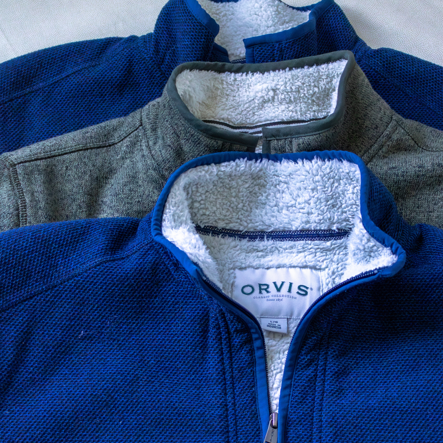 Folded jackets in blue and green with white sherpa lining, featuring the Orvis brand.