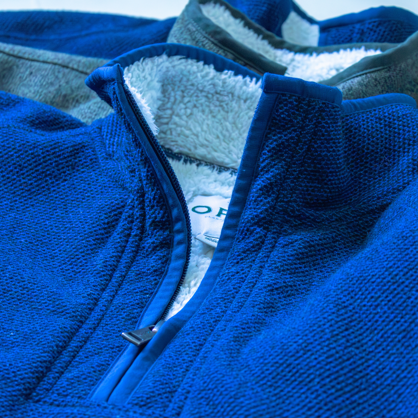 Close-up of a blue fleece jacket with a Orvis logo on a white background