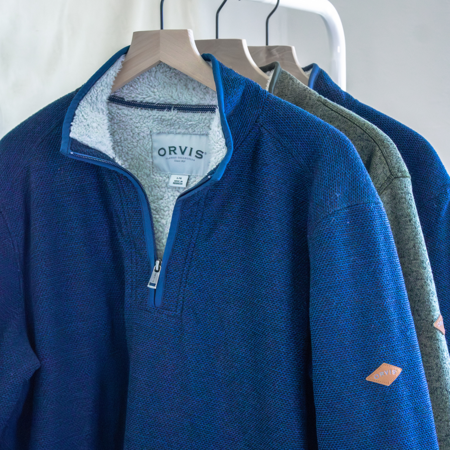 Blue and green pullovers hanging on a rack with 'Orvis' branding.